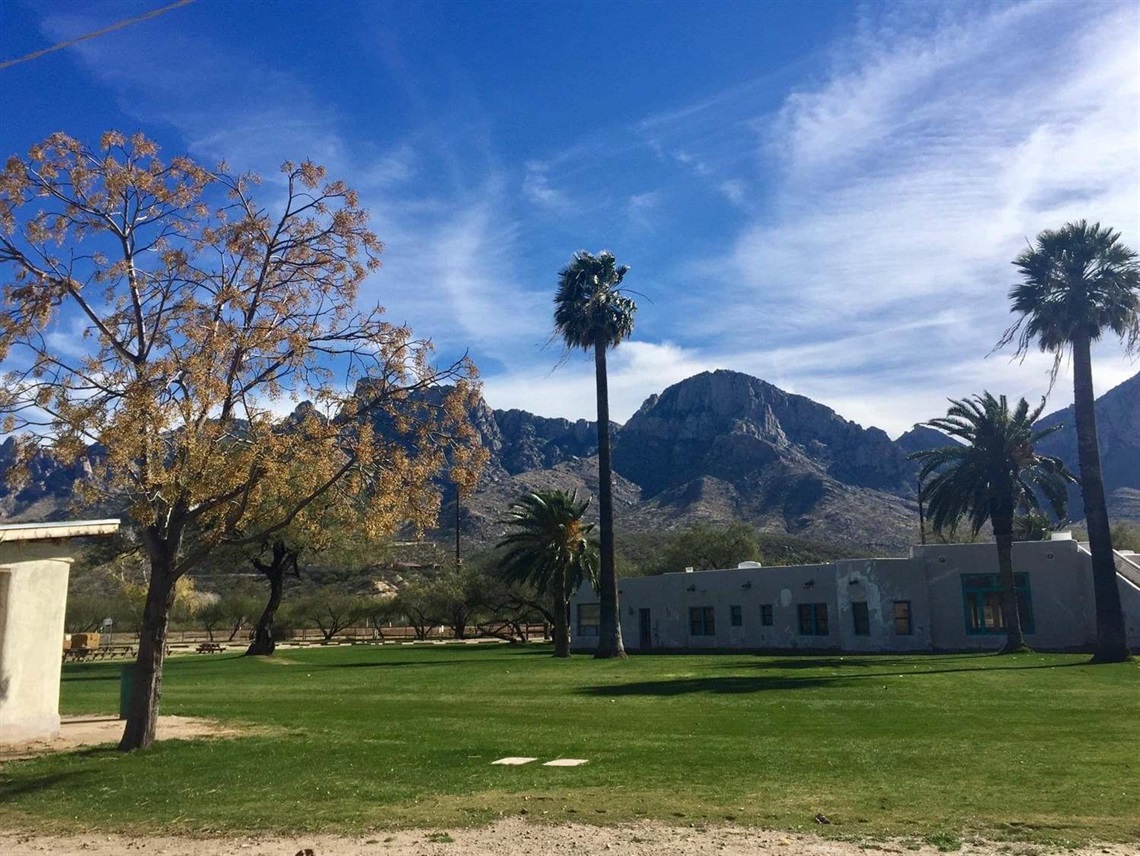 Two horse riders, trees and old buildings at Steam Pump Ranch with Pusch Ridge mountain in background