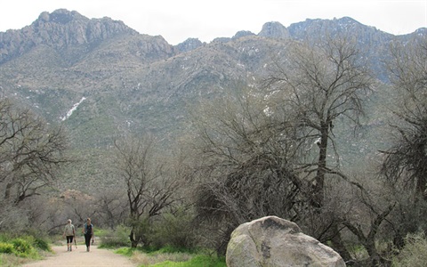 Two hikers in the distance walking a trail with moutains in background