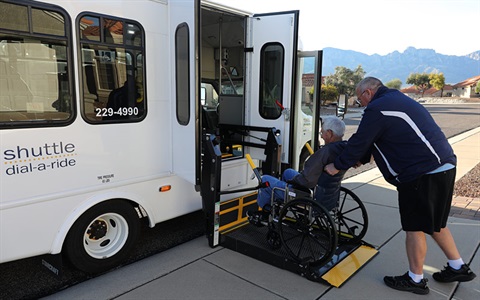 Driver loading rider in wheelchair onto Sun Shuttle van