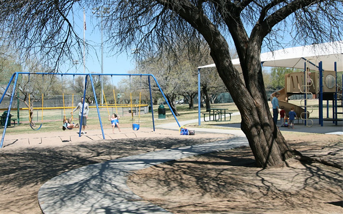 Kids playing on swings and playground equipment beneath shade of tree at James D. Kriegh Park