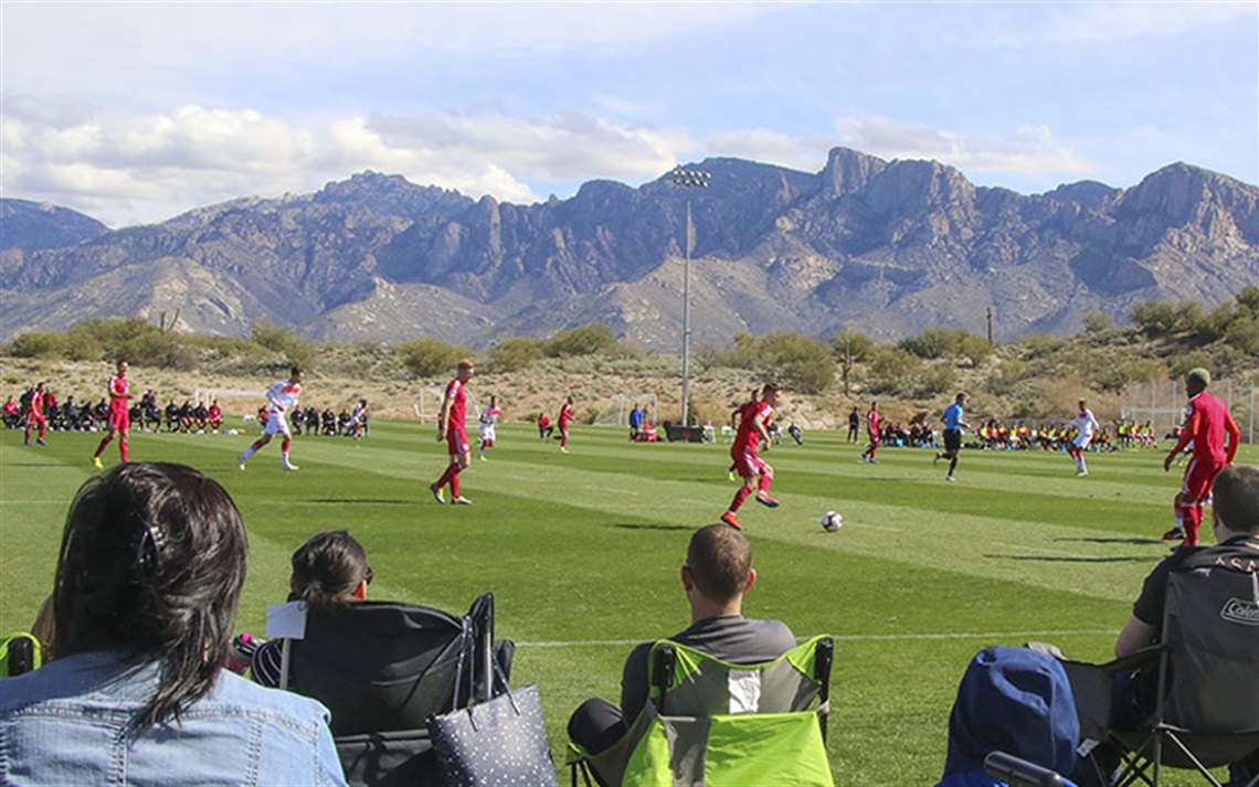 Spectators watching soccer game at Naranja Park with Catalina Mountains in background