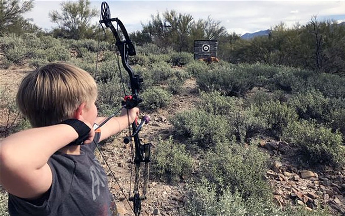 Youth aiming arrow at target with desert foliage in background
