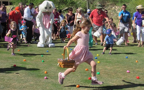 Little girl with basket skips to gather eggs with easter bunny and group of people in background